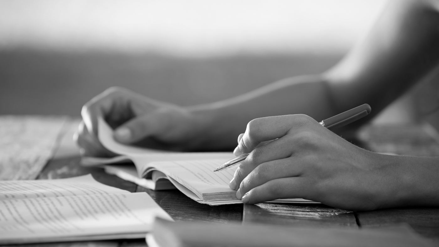 A writer working in a notebook alongside open books